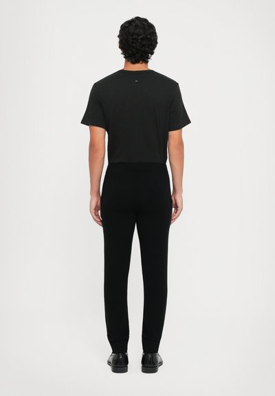 Fekete, rövid ujjú póló és szűkített nadrág, mindkettő puha anyagból készült. Az öltözet minimalista dizájnnal rendelkezik, és zökkenőmentes derékrésze van.