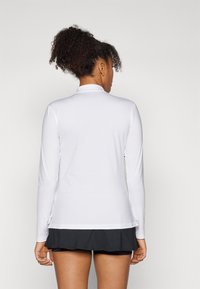 Camicia bianca a maniche lunghe con una texture a coste, dotata di colletto alto e spacchi laterali, abbinata a una gonna nera a strati.