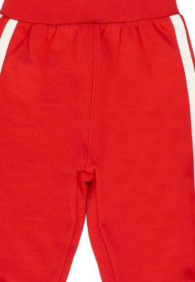 Pantaloni della tuta rossi con strisce verticali bianche sui lati esterni e una vita elastica, realizzati in un tessuto morbido.
