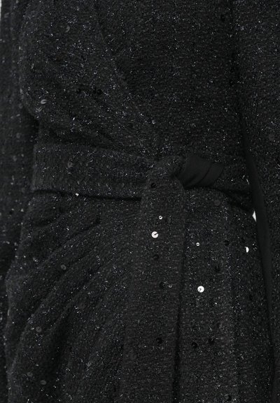 Melnas fakturētas audums ar spīdumiem, ar jostas saistīšanas detaļu. Materiāls šķiet mīksts un viegli mirdzošs, pastiprinot tā smalko dizainu.