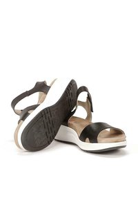 Sandalias de cuero negro con correas anchas en los dedos, una correa en el tobillo y una suela de plataforma blanca. Textura antideslizante en la suela negra.