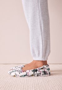 Lillamustriga kangast sussid, millel on pehme, pehmendusega tallaosa ja ümardatud nina. Kantud koos helehallide sooniliste pahkluumõõduliste pükstega.