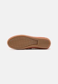 Suola di scarpe in gomma marrone con un motivo testurizzato, caratterizzata da impugnature circolari e un bordo liscio. Design leggero e forma flessibile.