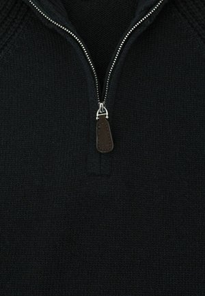 Mustat neulehuppari, jossa on vetoketjullinen kaulus, hopeiset yksityiskohdat ja ruskea nahka-aksoni vetoketjun vetimessä.