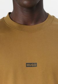 Brun bomull T-skjorte med rund hals og en liten svart "HUGO" logo på brystet. Jevn tekstur med en tettsittende design.