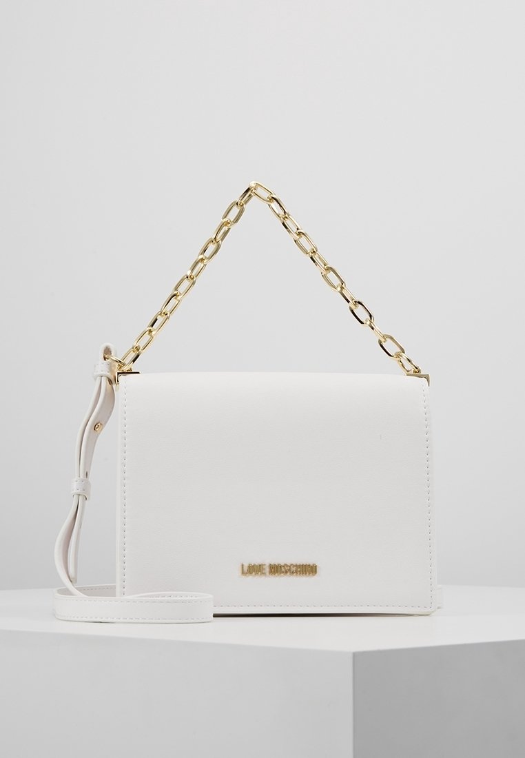 Vit konstläder handväska med en guld kedjeslinga, rektangulär form och en guld logotypaccent framtill. Slät textur, minimalistisk design.