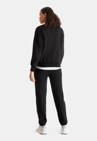 Black sweatshirt and joggers set, featuring a relaxed fit, ribbed cuffs, and a soft texture. Sneakers complete the outfit.