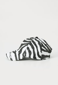 Black and white zebra-striped baseball cap with a curved brim, fabric texture, and adjustable strap at the back. "Couture" printed on the brim.