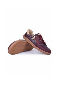 Paire de chaussures décontractées en cuir bordeaux avec des accents beiges au talon, fermeture éclair rouge sur le côté, semelles en caoutchouc marron et lacets bordeaux assortis.