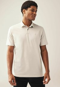 Polo de color gris claro hecho de una tela suave, con un collar clásico, mangas cortas y un sutil logo en el pecho.