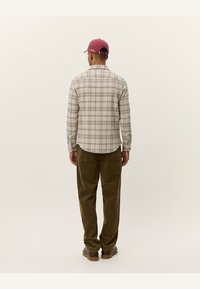 Plaid flannel shirt in beige tones with green accents, featuring a button-down collar and long sleeves, worn with olive corduroy trousers.