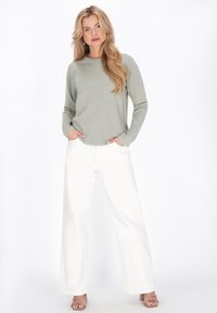 Pull côtelé vert clair avec motif texturé, associé à un pantalon blanc à jambes larges. Le modèle porte des sandales à talons beige et a les mains dans les poches.