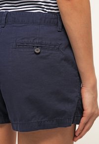 Pantalones cortos de algodón azul marino con un bolsillo trasero con botón, ajuste entallado y textura suave, con dobladillo limpio y diseño minimalista.