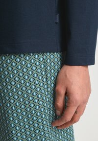 Marineblauw lang shirt met ribbeltextuur, gecombineerd met groene broek met een patroon van blauw en witte diamantvormen.