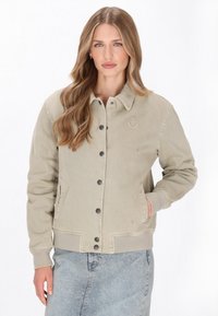 Beige színű corddzseki, gallérral, gombos záródással és hímzett horgony részlettel. Jellemzője a bordázott mandzsetta és az egyenes fazon.