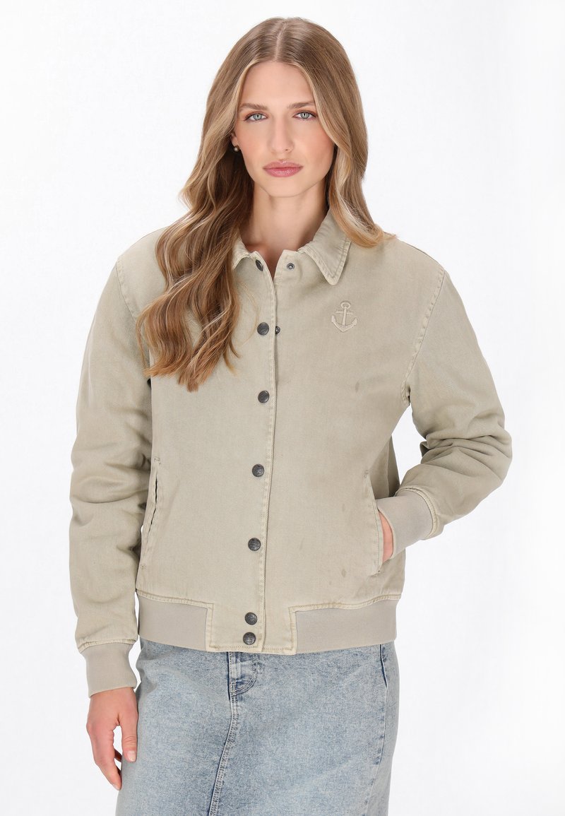 Beige színű corddzseki, gallérral, gombos záródással és hímzett horgony részlettel. Jellemzője a bordázott mandzsetta és az egyenes fazon.