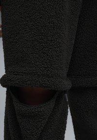 Giacca in pile nero peloso con colletto alto e tasche laterali con zip, caratterizzata da una superficie texturizzata e una vestibilità comoda.