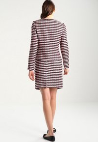 Kniejurk met roze en zwarte ruitpatroon, lange mouwen, ronde halslijn en aansluitende pasvorm. Stof lijkt een textuur te hebben.