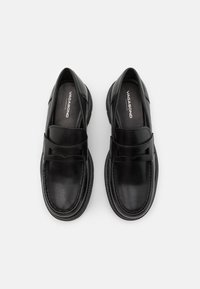 Juodos odos loaferiai su lygiu paviršiumi, su plačia juosta per priekį ir apvaliu pirštu. Be raištelių, tvirti padai.