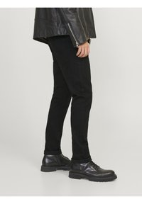 Černé slim-fit džíny spárované s černými šněrovacími botami. Džíny mají klasický pětikapsový styl a hladkou texturu.