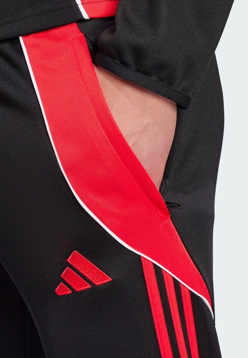 Pantalons de sport noirs avec des panneaux latéraux rouges et un biais blanc. Comprend un logo rouge brodé et une poche sur le côté.