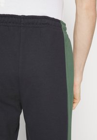 Black and green joggers made of soft fabric, featuring an elastic waistband and a side panel in dark green, with a smooth texture.