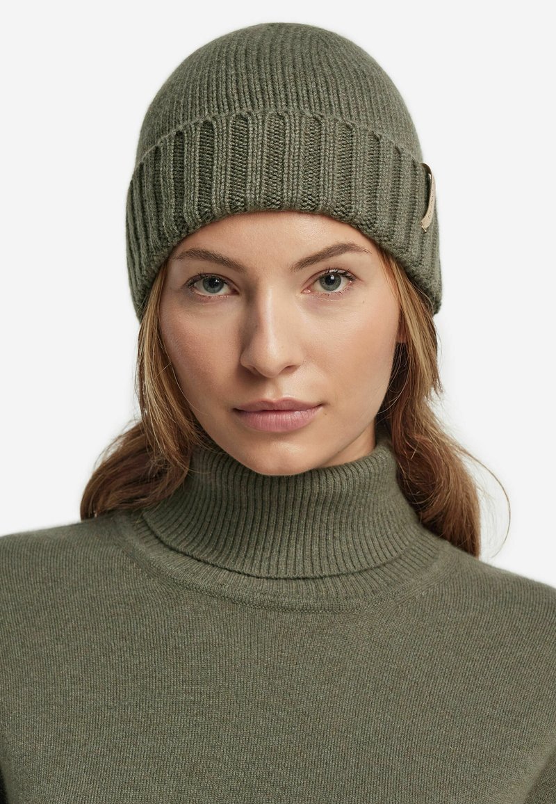 Olivgrön stickad mössa med ribbat mönster, försedda med en liten accentetikett. Matchad med en olivgrön ribbad polotröja.