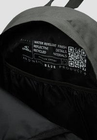 Interior gris de una mochila con acabado repelente al agua. Las características incluyen detalles reflectantes, una etiqueta con código QR y materiales reciclados.