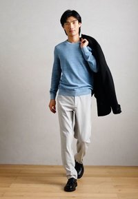 Ανοιχτό μπλε πουλόβερ με υφή, συνδυασμένο με ανοιχτό γκρι παντελόνι και μαυρες παπουτσες; μαύρο σακάκι περασμένο στον ώμο.