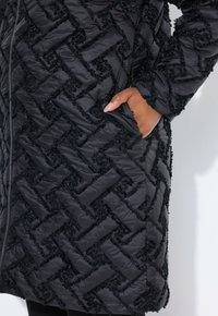 Svart puffjacka med texturerat zick-zackmönster. Har en framzipper och sidofickor, tillverkad av slätt, isolerat material.