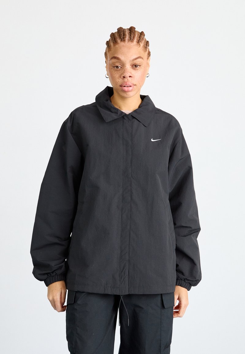 Juodas vėjo neperpučiamas džemperis su apykakle, elastingais rankogaliais ir subtilia logo ant krūtinės. Patvari medžiaga su šiek tiek tekstūruota apdaila.