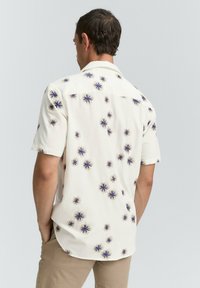 Kurzes, cremefarbenes Hemd mit einem floralen Muster in Dunkelblau und Hellbraun. Der Stoff wirkt leicht und hat eine glatte Textur.