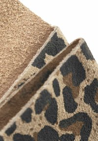 Twee lagen suede, de ene in lichtbeige en de andere met een zwart en bruin luipaardprintpatroon, waarbij textuur en materiaaldetails zichtbaar zijn.