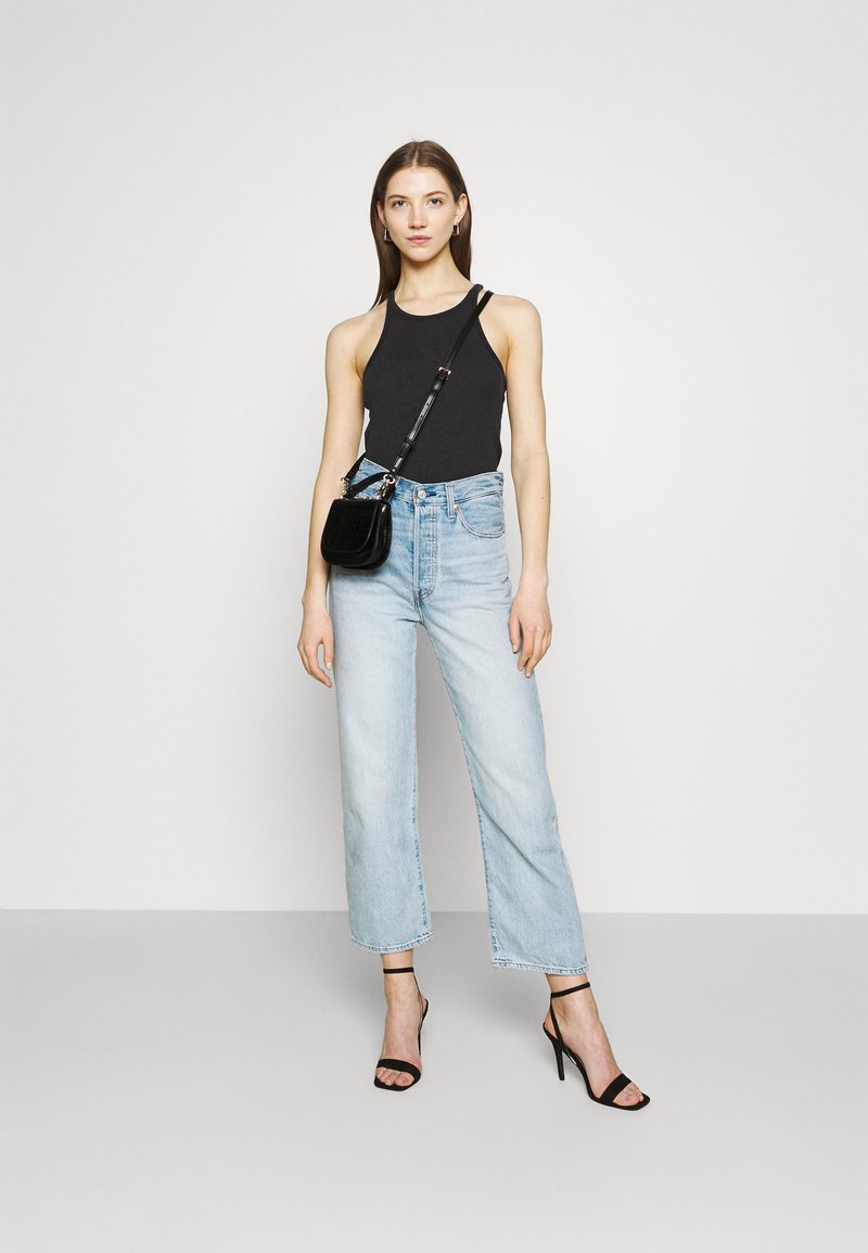 Czarny top bez rękawów, jasnoniebieskie szerokie dżinsy, czarna torba na ramię, czarne sandały na obcasie. Minimalistyczny design w casualowym stylu.