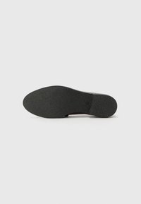 Semelle de chaussure en caoutchouc noir avec une surface texturée et un bout rond. Présente une légère courbure au niveau du talon et des bords lisses pour le confort.