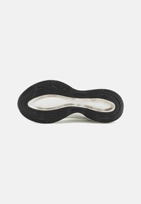 Suola di scarpa da ginnastica in bianco e nero caratterizzata da gomma testurizzata per una migliore aderenza, forma curvata e distintivi modelli di battistrada per una trazione migliorata.