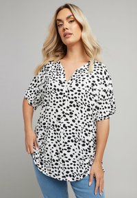 Camicia bianca e nera con vestibilità ampia, caratterizzata da un motivo a pois, maniche corte e orlo curvo. Tessuto testurizzato.