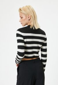 Zwart-wit gestreepte cropped trui met lange mouwen en een ronde hals, met een zachte textuur en ribbelzoom. Gecombineerd met zwarte broek.