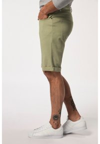 Pantaloni corti in cotone verde chiaro con una vestibilità slim, risvolti e tasche laterali. Abbinati a sneakers bianche. Texture liscia e design casual.