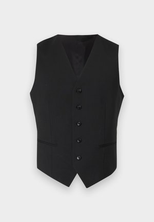 Uomo con camicia azzurra chiara, gilet nero, pantaloni grigi, scarpe nere che tiene una valigetta nera su sfondo bianco semplice.