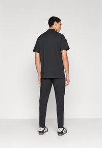 Μαύρο μπλουζάκι με κοντά μανίκια, λεία υφή, φαρδιά εφαρμογή. Συνδυάζεται με σκούρες φόρμες jogging με σχεδιασμό στενής γραμμής στα πόδια και μαύρα αθλητικά παπούτσια.