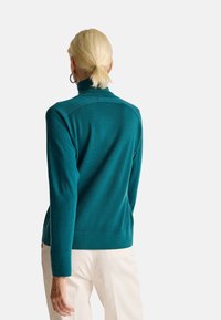 Türkisfarbener Strickpullover mit hohem Kragen. Verfügt über eine glatte Textur und gerippte Bündchen, entworfen für einen figurbetonten Schnitt in der Taille.