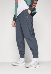 Pantaloni cargo grigi scuri con polsini elastici, dotati di una tasca laterale e di un'etichetta con logo. Abbinati a scarpe da ginnastica bianche e a una giacca colorata.