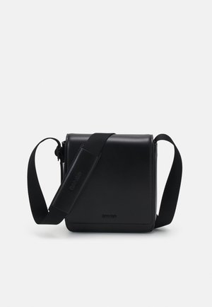 Sac bandoulière noir en cuir lisse, de forme rectangulaire, avec une sangle ajustable et un logo sur le devant.