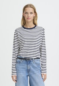 Chemise à manches longues blanche avec des rayures horizontales bleu marine, dotée d'un col rond et d'une coupe décontractée. Associée à un jean denim bleu taille haute.