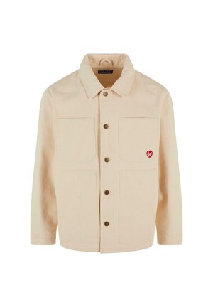 Light beige jacket made of canvas with a collar, front button closure, two wide chest pockets, and a small red logo on the left pocket.