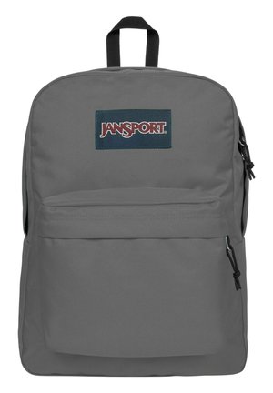 Sac à dos Jansport gris avec un grand compartiment principal, une poche avant et des bretelles réglables. Présente un écusson bleu sur le devant.