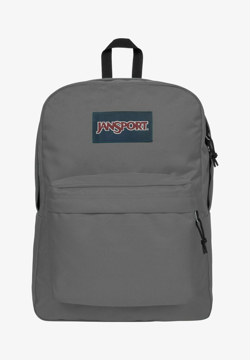 Sac à dos Jansport gris avec un grand compartiment principal, une poche avant et des bretelles réglables. Présente un écusson bleu sur le devant.