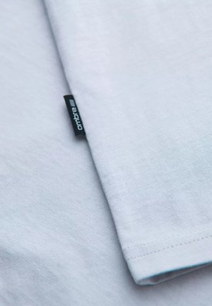 T-shirt in cotone azzurro chiaro con una texture liscia, maniche corte e un'etichetta "ombre" cucita di lato.