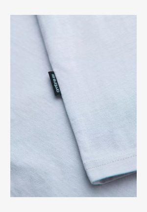 Lyseblå bomulds t-shirt med en glat tekstur, korte ærmer og et "ombre"-mærke syet på siden.